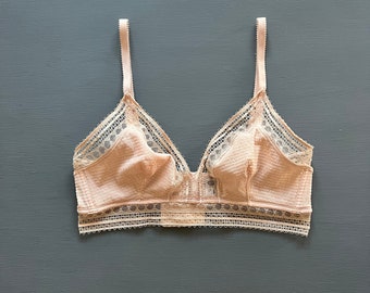 May include: A delicate, pale pink lace bra with adjustable straps. The bra has a scalloped lace trim and a V-shaped neckline.