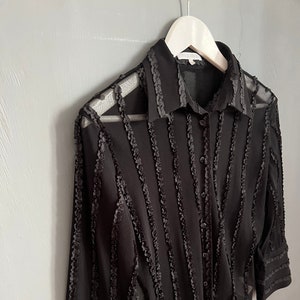 May include: Black sheer button-up shirt with ruffled trim and long sleeves.