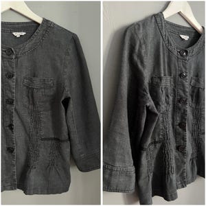 Può includere: Una giacca di jeans grigio scuro con colletto alla coreana, chiusura con bottoni e due tasche a patta. La giacca presenta un dettaglio plissettato sul davanti ed è realizzata in un tessuto morbido e confortevole.