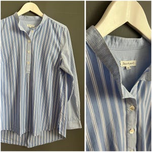 May include: A blue and white striped long-sleeved shirt with a mandarin collar and button closure. The shirt has a Jackpot label on the collar.