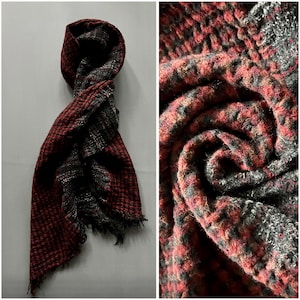 Może przedstawiać: Czerwono-czarny szal w kratę z frędzlami. Szal wykonany jest z miękkiej, fakturowanej tkaniny.