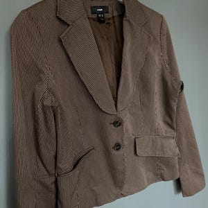 K&ouml;nnte beinhalten: Ein brauner Blazer mit wei&szlig;en Streifen, zwei Kn&ouml;pfen und einer Tasche auf der linken Seite. Der Blazer ist von H&M.