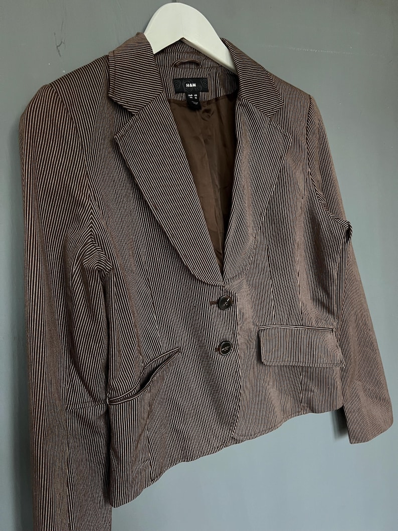 K&ouml;nnte beinhalten: Ein brauner Blazer mit wei&szlig;en Streifen, zwei Kn&ouml;pfen und einer Tasche auf der linken Seite. Der Blazer ist von H&M.