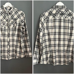 Może przedstawiać: Koszula w biało-czarną kratę z długimi rękawami i guzikami, z haftowanym napisem "Harley Davidson" na plecach.