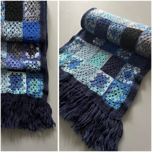 Peut inclure: Une couverture en crochet bleu et blanc avec une bordure en franges. La couverture est faite de carrés dans différentes nuances de bleu et de blanc.