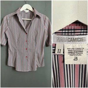 May include: A short-sleeved, striped button-down shirt with a pink, white, and black color scheme. The shirt has a label that reads "NARACAMICIE II PER UNA CORRETTA MANUTENZIONE E' OBBLIGATORIO LO STIRO A BASSA TEMPERATURA a".