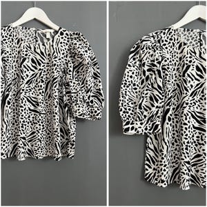 May include: A white and black animal print blouse with a round neckline and puffed sleeves.
