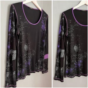 May include: Black long-sleeved shirt with a purple trim and a print of text and abstract shapes. The text includes "Coyote London Gar", "Girls", and "CG".