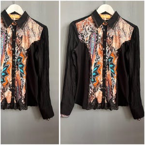 May include: Black long-sleeved shirt featuring a vibrant paisley pattern on the front and sleeves. The shirt has a button-down front and a black collar. The paisley design incorporates orange, blue, and purple hues. The shirt is displayed on a white hanger.