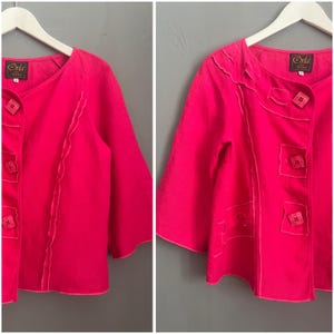Pode incluir: Uma jaqueta rosa de manga curta com costuras decorativas e botões. A jaqueta tem um decote redondo e é feita de um tecido leve. O rótulo na jaqueta diz "Orla."