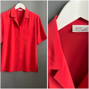 Op de afbeelding: Een felrood overhemd met korte mouwen, een knoopsluiting en een enkele borstzak. Het overhemd hangt aan een witte hanger. Het label luidt "BASLER".