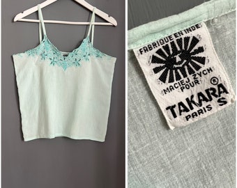 Puede incluir: Un top sin mangas de color verde claro con un escote bordado en turquesa. El top tiene una etiqueta blanca con el texto "Fabrique en Inde" y "Maciej Zych pour Takara Paris".