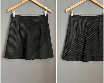 May include: Two black skirts with diagonal pinstripes hanging on wooden hangers. One skirt is a mini skirt with a flared shape. The other skirt is a pair of shorts with a button closure.