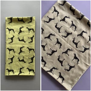 May include: Two fabric squares with a repeating pattern of black silhouettes of greyhounds. One square is a light yellow color and the other is a light beige color.