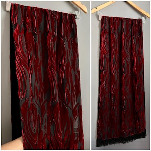 Puede incluir: Una bufanda de terciopelo rojo y negro con un patrón de llama. La bufanda tiene una franja negra en la parte inferior.