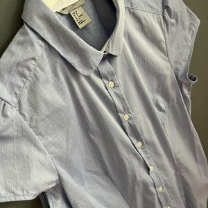 Op de afbeelding: Een lichtblauw overhemd met korte mouwen en een witte kraag. Het overhemd is voorzien van knopen en heeft een subtiel stippenpatroon. De knopen zijn wit.