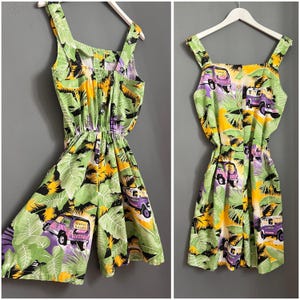 May include: A green, yellow, and purple sleeveless dress with a tropical print featuring palm trees and small cars. The dress has a drawstring waist and a relaxed fit.
