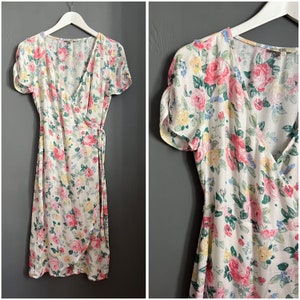 May include: A white wrap dress with a floral print featuring pink, red, and yellow roses. The dress has short sleeves and a V-neckline.