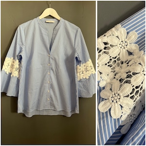 May include: A blue and white striped button-up shirt with white lace trim on the sleeves.