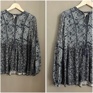 Op de afbeelding: Een marineblauwe blouse met lange mouwen en een bloemen- en geometrisch patroon. De blouse heeft een ronde hals met een kwastje, een gerimpelde taille en uitlopende mouwen. De stof heeft een zacht, vloeiend uiterlijk.