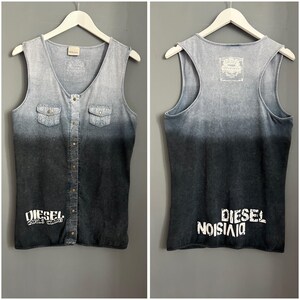 Pode incluir: Uma camisa sem mangas preta e azul com um visual de jeans desbotado. A frente da camisa tem um fecho de botões e dois bolsos. As costas da camisa têm o texto "DIESEL DIVISION" impresso em branco.