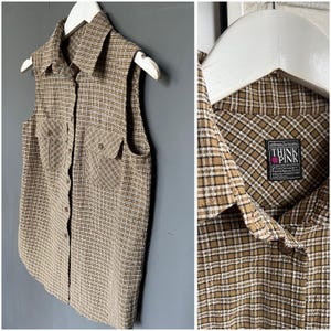 Può includere: Camicia senza maniche a quadri marrone e bianca. La camicia ha due tasche frontali e un colletto. L'etichetta all'interno della camicia dice "THINK PINK". La camicia è appesa a una gruccia bianca.