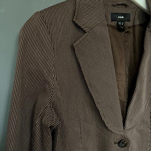 K&ouml;nnte beinhalten: Ein brauner Blazer mit wei&szlig;en Nadelstreifen und einem einzigen Knopfverschluss. Der Blazer hat einen Schalkragen und zwei Pattentaschen. Das Etikett auf dem Blazer lautet "H&M".