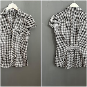 May include: A black and white gingham print button-down shirt with short sleeves. The shirt has two chest pockets and a classic collar. The back of the shirt has a gathered waist detail. The shirt is hanging on a white hanger.