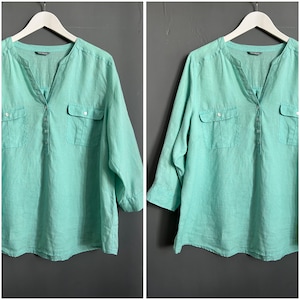 Może przedstawiać: Jasnozielona koszula lniana z zapięciem na guziki, dwiema kieszeniami na piersi i rękawami trzy czwarte.