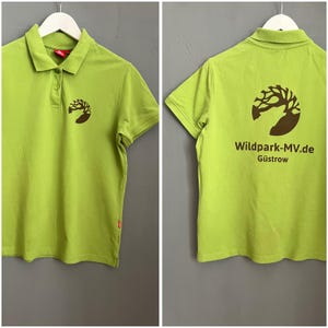 May include: A lime green polo shirt with a brown logo on the front and back. The logo features a tree with a deer inside a circle. The text "Wildpark-MV.de Güstrow" is printed below the logo on the back.