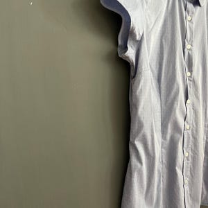 Op de afbeelding: Lichtblauw overhemd met knopen en korte, gefranjerde mouwen. Het overhemd heeft een subtiel stippenpatroon en een ronde kraag. De stof lijkt licht van gewicht, geschikt voor warmer weer. Het overhemd is aan de voorkant dichtgeknoopt.