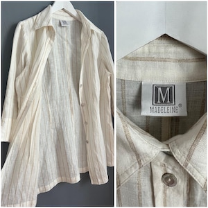 May include: A white linen shirt with thin brown stripes and a button-up front. The shirt has a label that reads "Madeline".