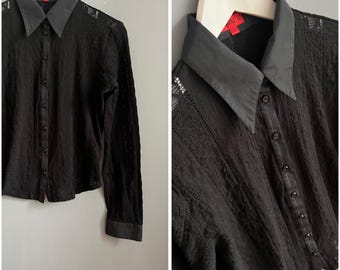 May include: Black button-down shirt with a contrasting black collar and cuffs. The shirt has a textured, open-weave design and is hanging on a white hanger against a gray background. The collar has a red tag.
