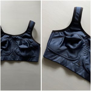 May include: A navy blue sports bra with black trim. The bra has wide straps and a full coverage design. The fabric has a slight sheen. The bra is designed for high-impact activities.