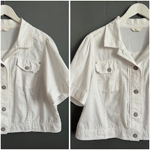 May include: White linen short-sleeved button-up shirt with a collar and two pockets. The shirt has a cropped length and a relaxed fit.