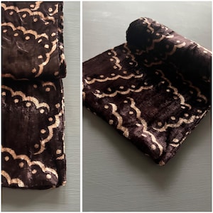May include: A brown velvet scarf with a cream-colored pattern of swirls and dots. The scarf is rolled up and lying on a gray surface.