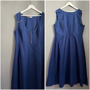 Peut inclure: Une robe bleue sans manches avec une patte de boutonnage blanche et une bordure verte. La robe a un dos plissé et une jupe légèrement évasée.