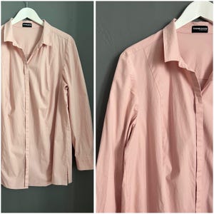 May include: A pale pink long-sleeved button-down shirt with a collar. The shirt has a brand label that reads "SAMOON" on the right side of the collar.