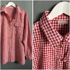 May include: Red and white gingham button-up shirt with small white floral print. The shirt has a collar and long sleeves. The label on the shirt reads "Landhaus, GSA Naturally".