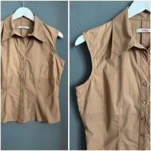 May include: A sleeveless, tan button-down shirt with vertical pinstripes. The shirt has a collared neckline and is hanging on a white hanger. The brand label "s.Oliver" is visible.