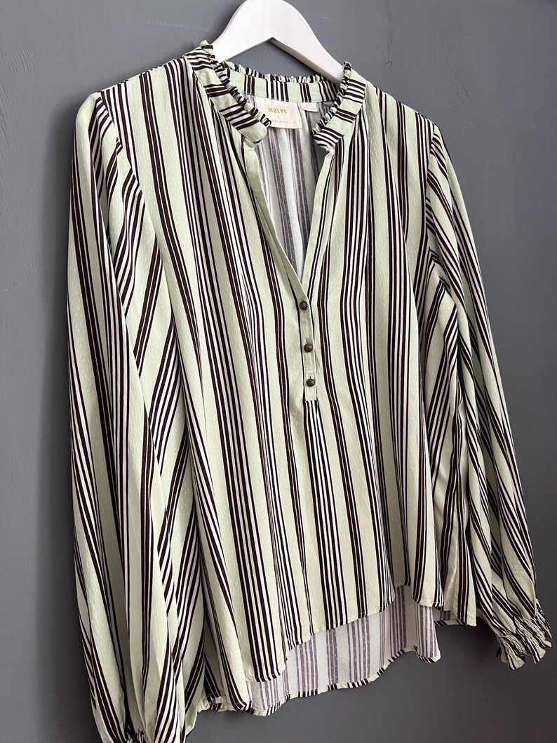 May include: A green and black striped long-sleeved blouse with a ruffled collar and a single button closure. The blouse has a slightly gathered hem.