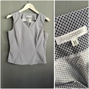 May include: A sleeveless blouse featuring a dark blue and white circular geometric pattern, a V-neckline, and a white hanger. The interior label displays the text NABACAMICIE and the number II, indicating the brand and size of the garment.