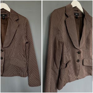 K&ouml;nnte beinhalten: Ein brauner Blazer mit wei&szlig;en Streifen, einem Reverskragen und Zwei-Knopf-Verschluss. Der Blazer hat zwei Eingrifftaschen und einen Schlitz am R&uuml;cken.