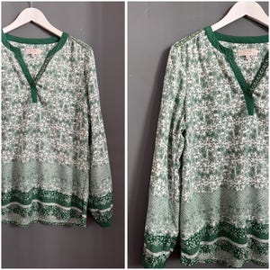 May include: A long-sleeved blouse with a green and white floral print, green trim and a v-neck. The blouse has a button closure at the neck.
