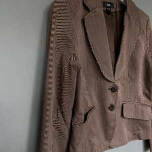 K&ouml;nnte beinhalten: Ein braunes und wei&szlig; gestreiftes Blazer mit einem einzigen Knopfverschluss und zwei Taschen. Der Blazer hat ein Etikett mit der Aufschrift "H&M" auf der Innenseite.