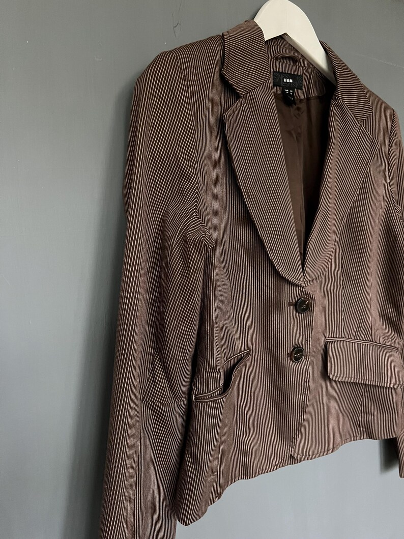 K&ouml;nnte beinhalten: Ein braunes und wei&szlig; gestreiftes Blazer mit einem einzigen Knopfverschluss und zwei Taschen. Der Blazer hat ein Etikett mit der Aufschrift "H&M" auf der Innenseite.