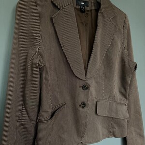 K&ouml;nnte beinhalten: Ein brauner Blazer mit wei&szlig;en Streifen, zwei Kn&ouml;pfen und einer Tasche auf der linken Seite. Der Blazer hat ein Etikett mit der Aufschrift "H&M".