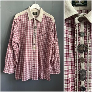 May include: A long-sleeve button-down shirt featuring a red and white plaid pattern, a beige collar, and a central placket adorned with various metallic decorative buttons. The shirt includes a label at the neck with the text Trachten.
