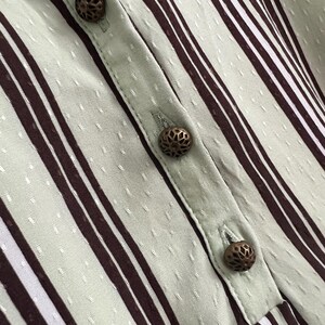 May include: Close-up of a light green and brown striped fabric with decorative metal buttons. The fabric has a subtle textured pattern.