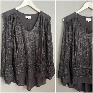Può includere: Un top nero senza maniche con paillettes, scollo a V e un orlo a balze sovrapposte.